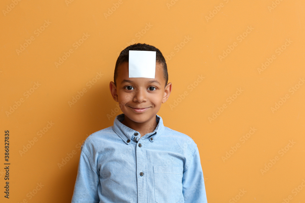 Little African-American boy with blank note paper on his forehead against color background