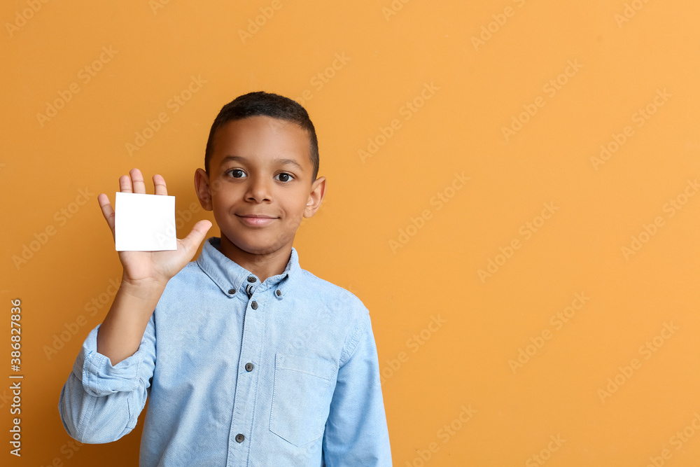 Little African-American boy with blank note paper on color background