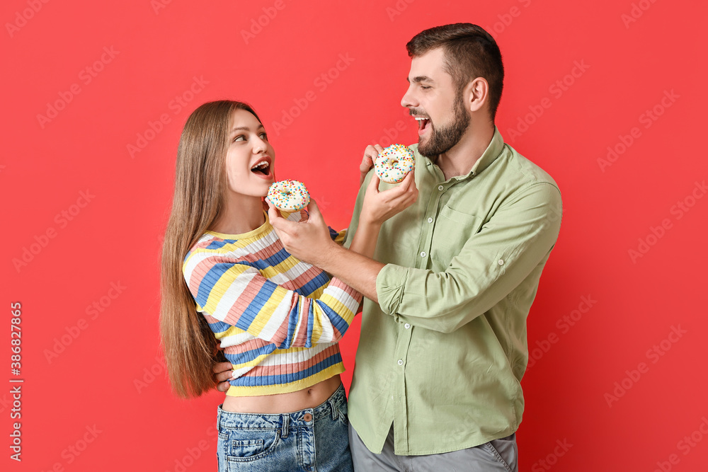 Young couple with sweet donuts on color background