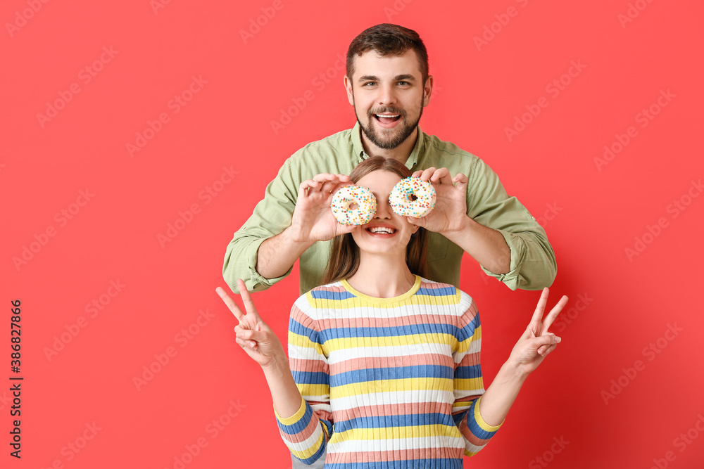 Young couple with sweet donuts on color background