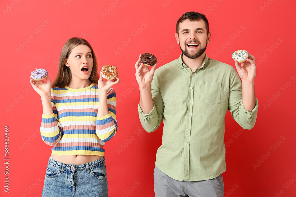 Young couple with sweet donuts on color background