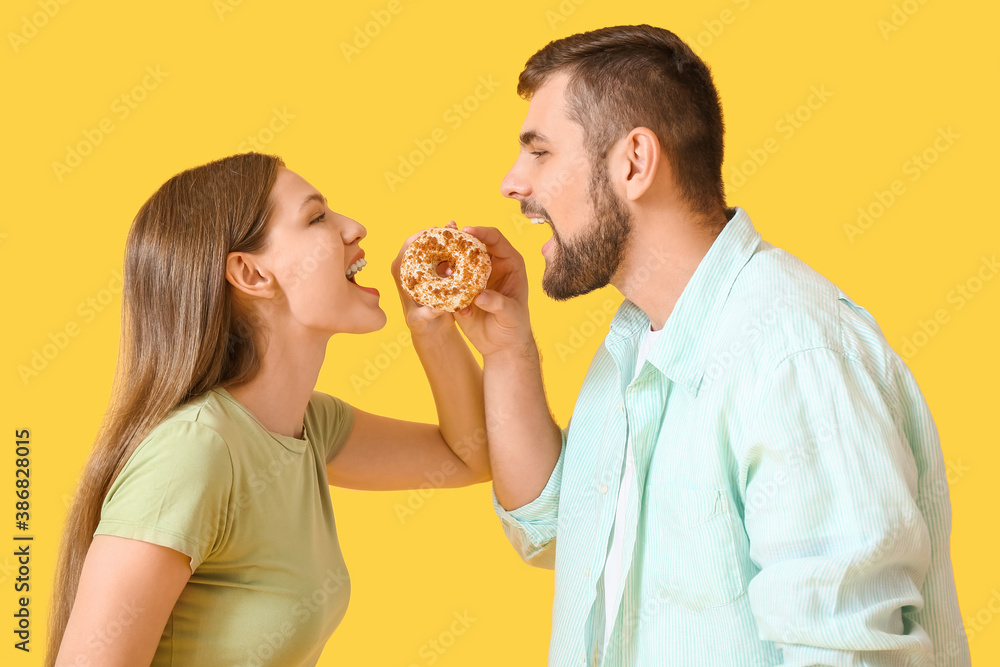 Young couple with sweet donut on color background