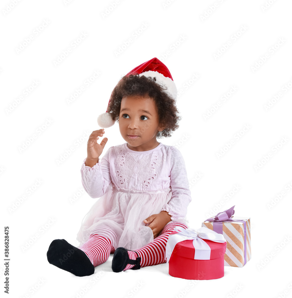 Cute African-American baby girl in Santa hat and with Christmas gifts on white background