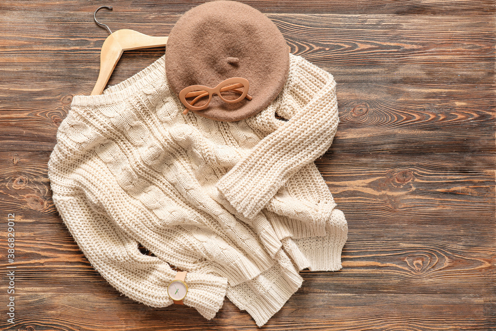 Clothes hanger with sweater, glasses and cap on wooden background