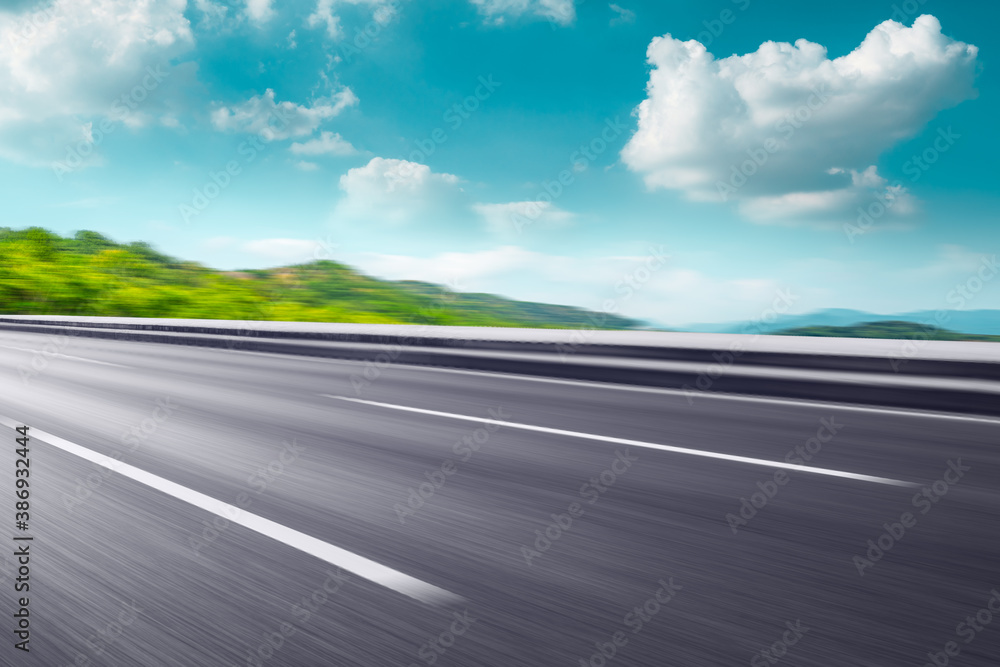 Motion blurred asphalt road and green mountain under blue sky.