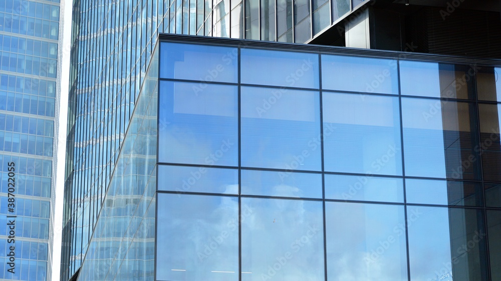 Blue curtain wall made of toned glass and steel constructions under blue sky. A fragment of a buildi