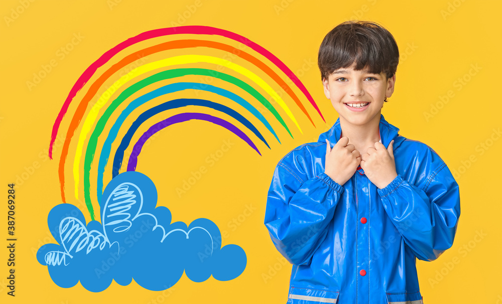 Cute little boy in raincoat on color background with drawn rainbow and cloud