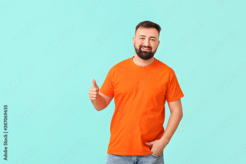 Handsome man in orange t-shirt showing thumb-up on color background