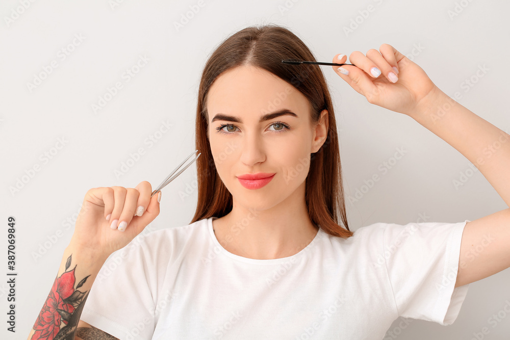 Young woman with tools for eyebrow correction procedure on light background