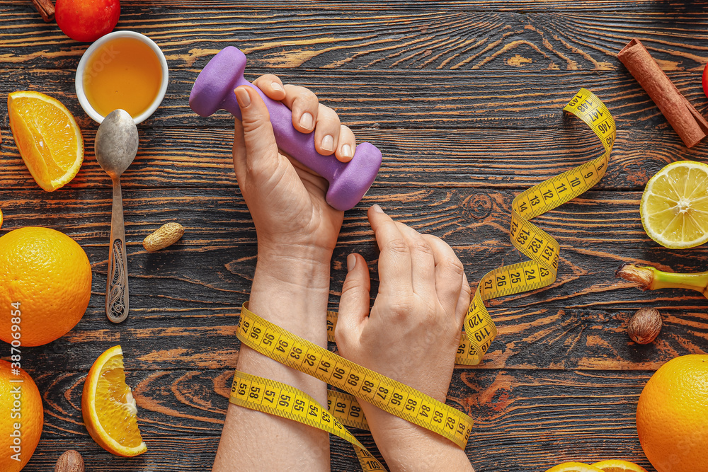 Female hands with measuring tape, dumbbell and fresh products on wooden background. Diet concept