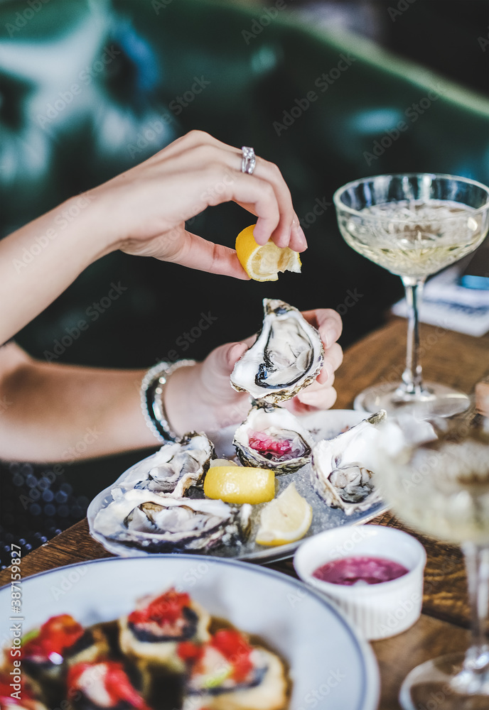 Hands of woman squeezing fresh lemon juice to Irish oyster over seafood and glass of champagne in fi