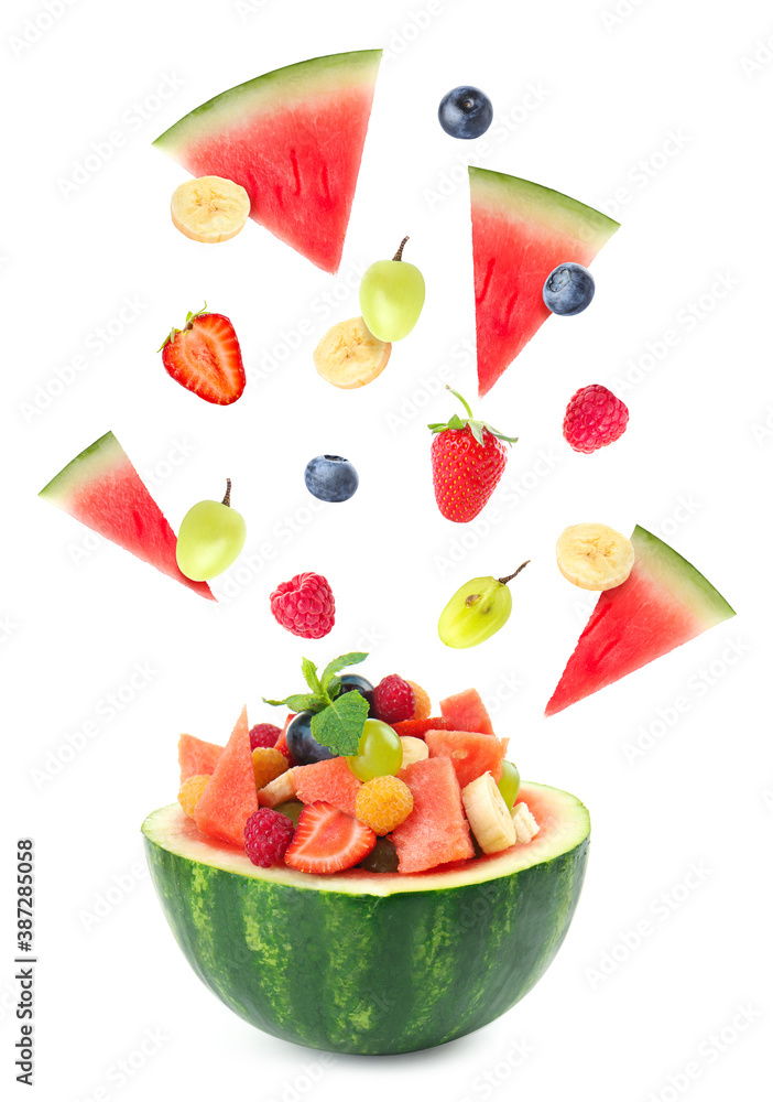 Delicious fruit salad in watermelon bowl with flying ingredients on white background