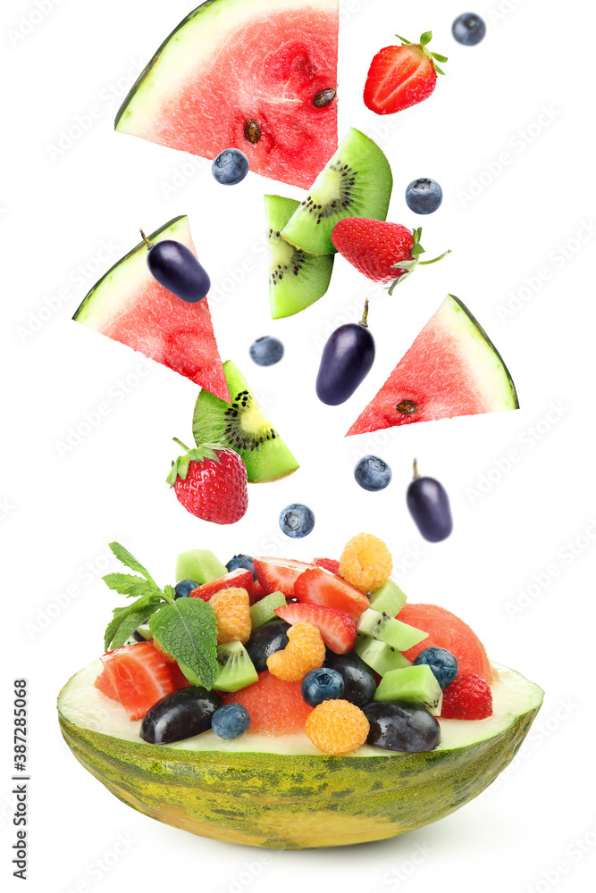 Delicious fruit salad in melon bowl with flying ingredients on white background