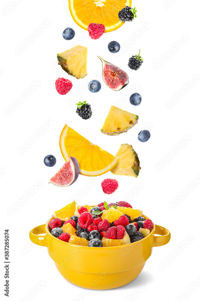 Delicious fruit salad in pot and flying ingredients on white background