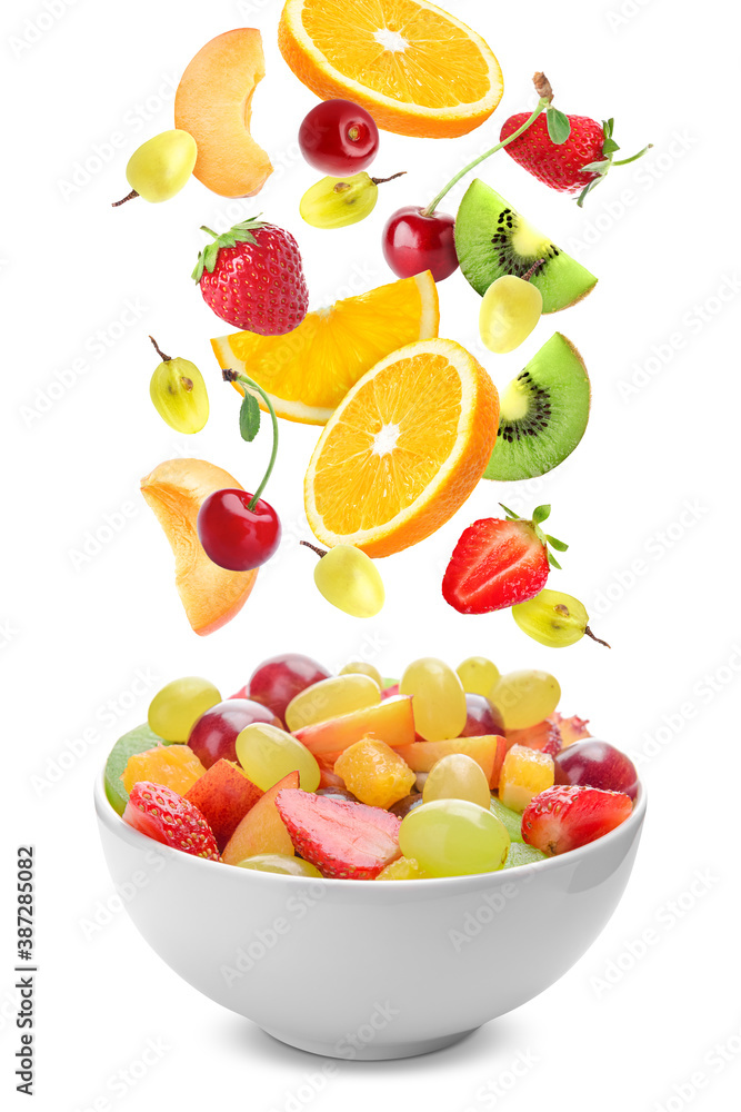 Delicious fruit salad in bowl and flying ingredients on white background