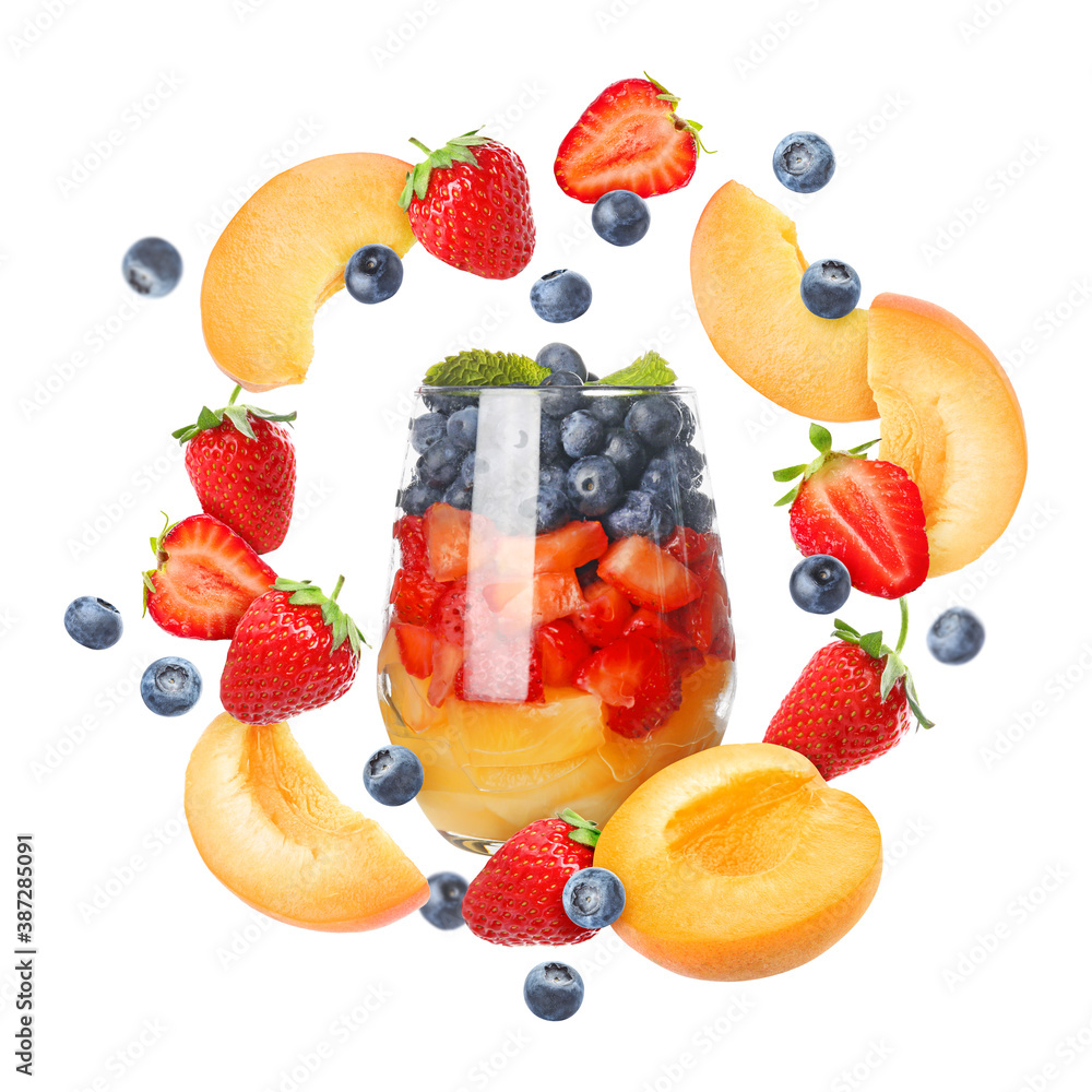 Delicious fruit salad in glass and flying ingredients on white background