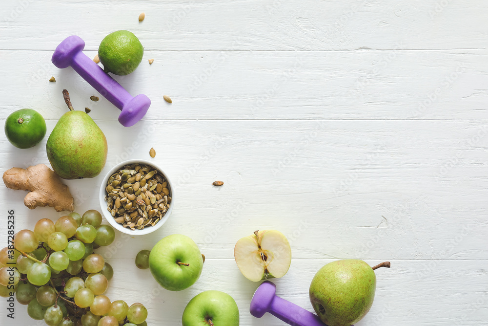 Fresh products and dumbbells on white wooden background. Diet concept