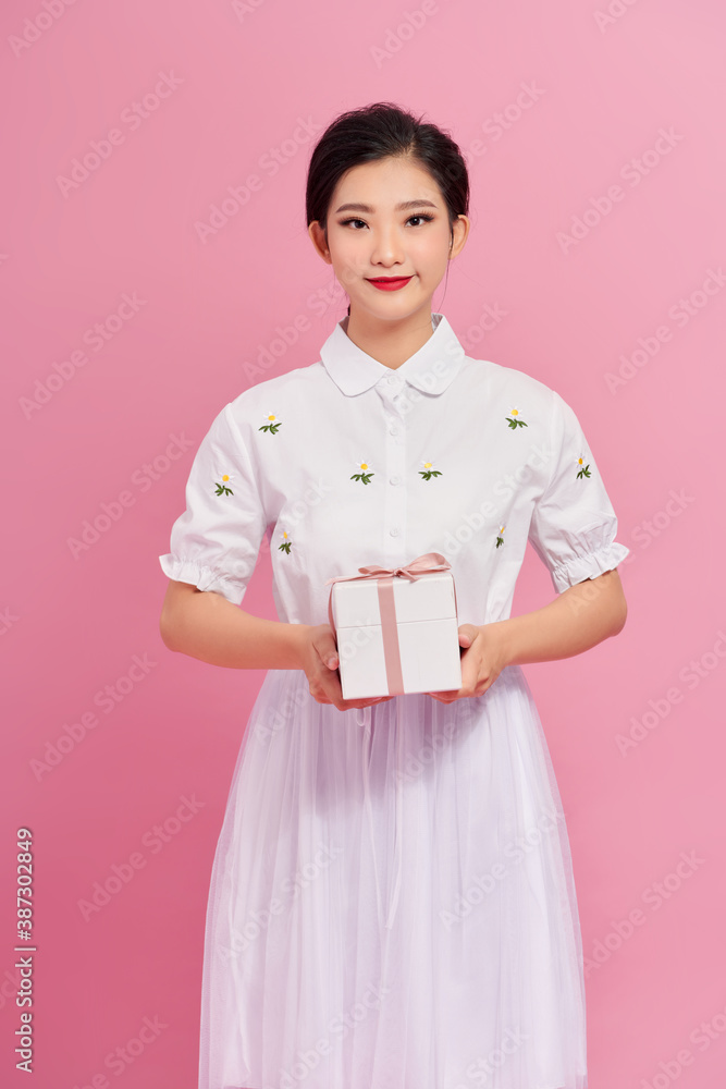 Portrait of a pretty smiling girl holding gift box and looking at camera isolated over pink backgrou