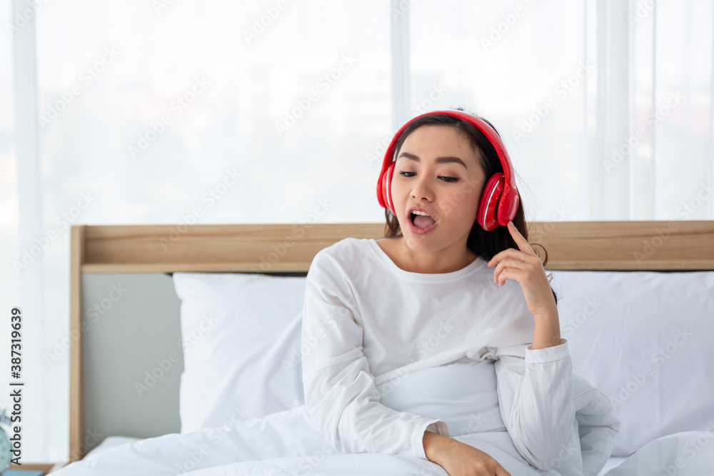 Happy woman female girl listening to music using headphones and smartphone on bed. Young woman or Te