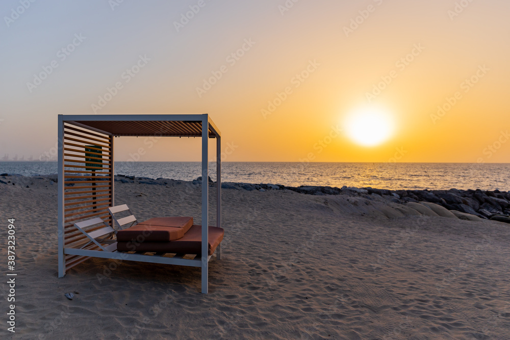 Empty double sun bed with pillows on the sandy beach in Dubai, with orange sunset in the background 