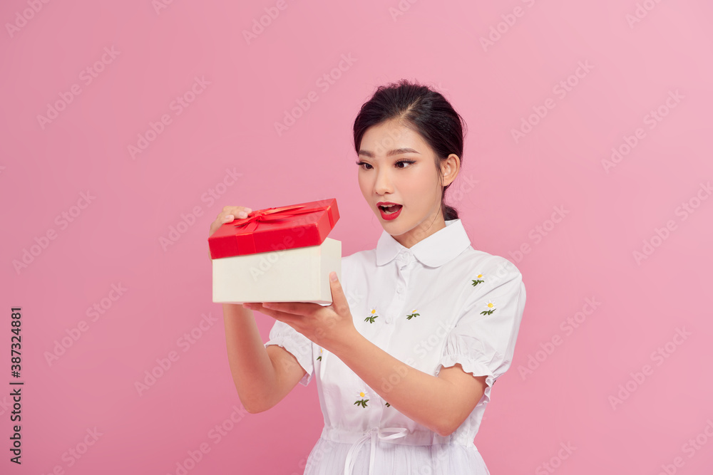 Surprised happy content curly young female looking inside present box on pink background