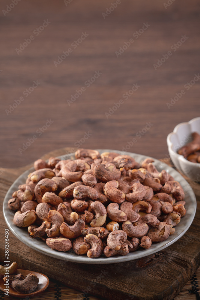 Cashew nuts with peel in a plate on wooden tray.