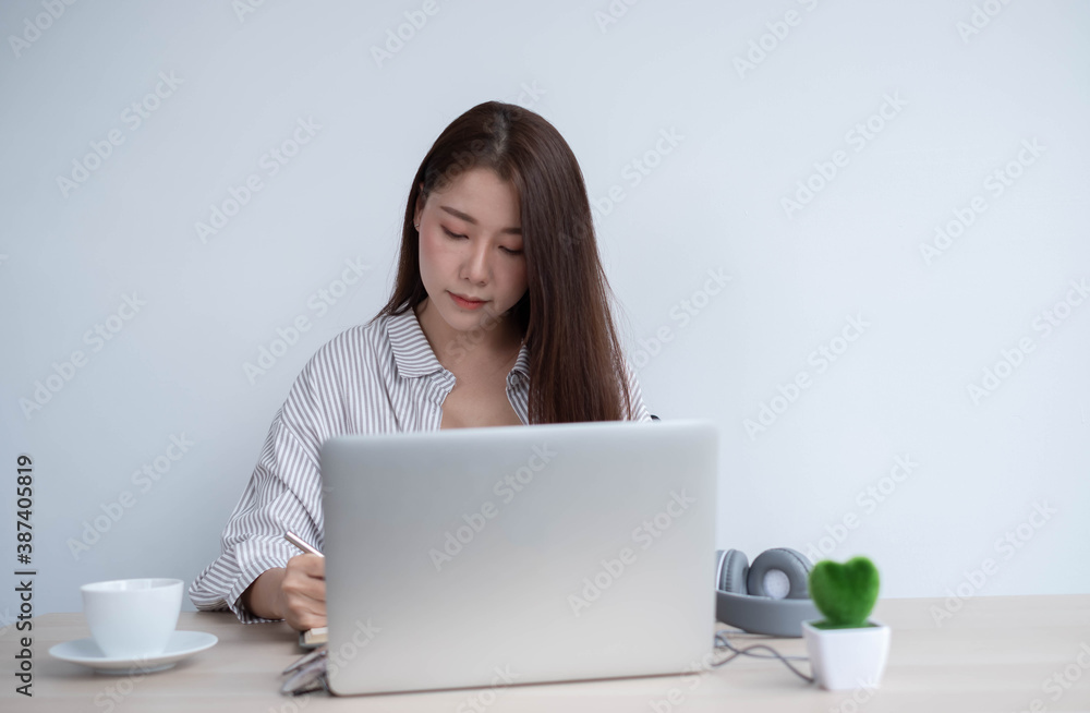 Young Asian women wear headphones using their laptop inside the office, working for online lessons o