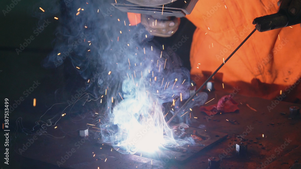 Metal welder working with arc welding machine to weld steel at factory while wearing safety equipmen