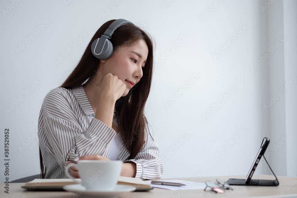 An Asian woman is wearing headphones and playing a tablet to communicate, listen to lectures, study 