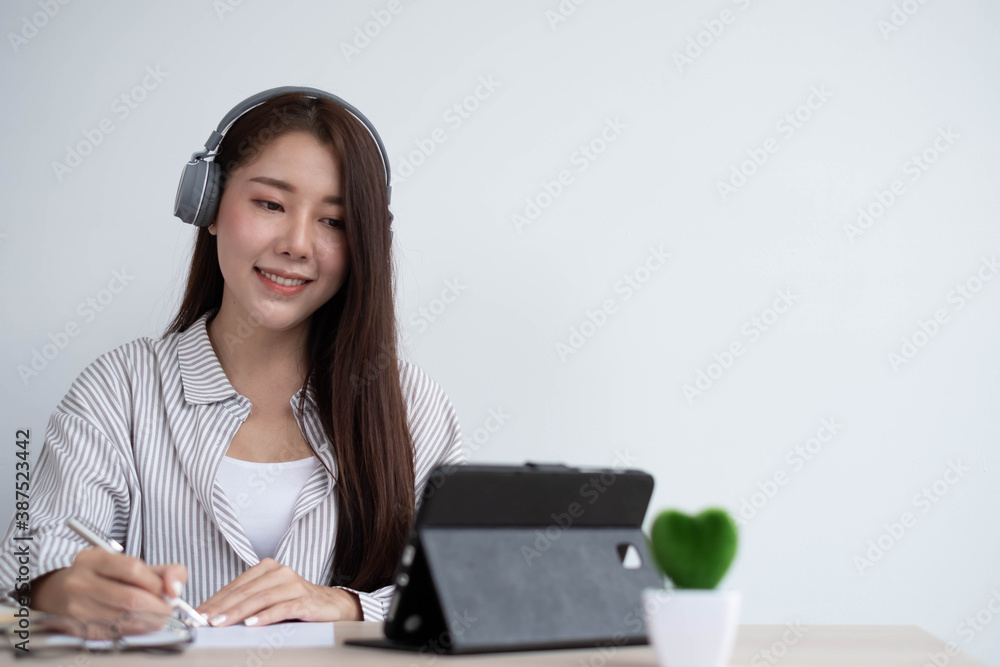 Young Asian women wear headphones to concentrate on studying remotely in their homes, meeting via vi