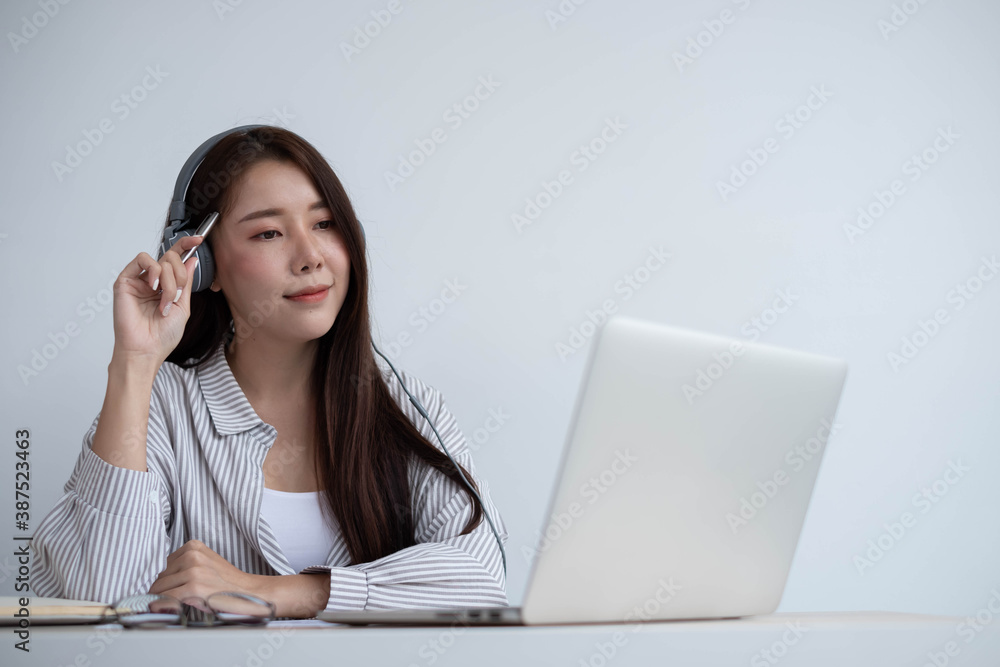 Young Asian women wear headphones to concentrate on studying remotely in their homes, meeting via vi