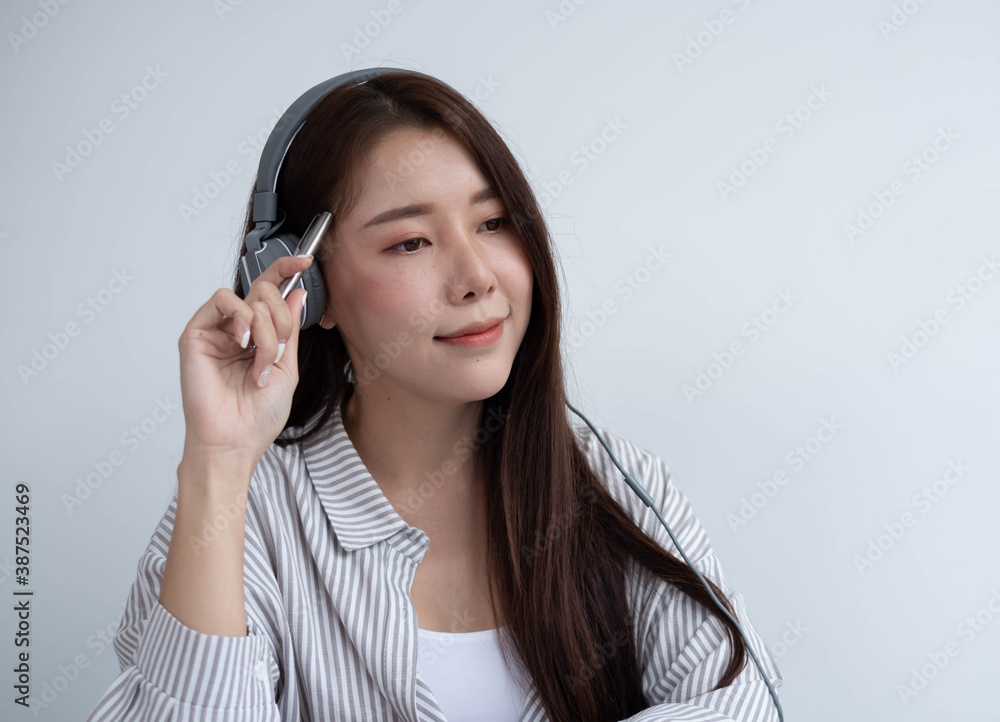 Portrait of an Asian woman wearing headphones to music or narration with her right hand holding a pe