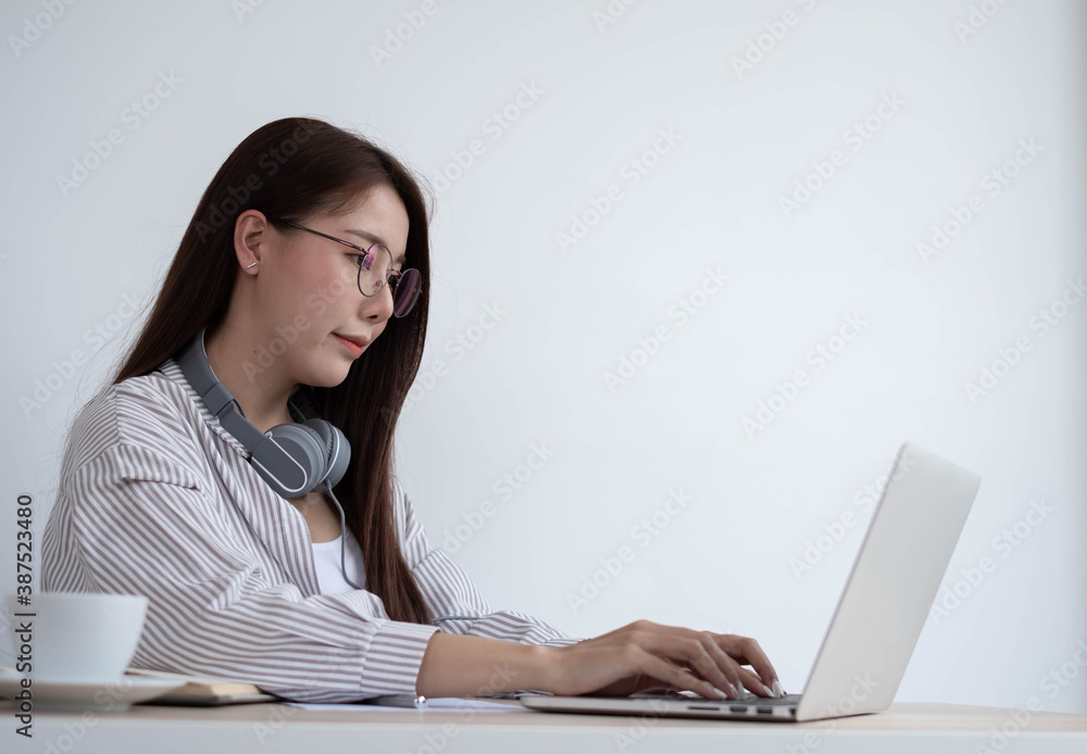 Young Asian women wear headphones using their laptop inside the office, working for online lessons o