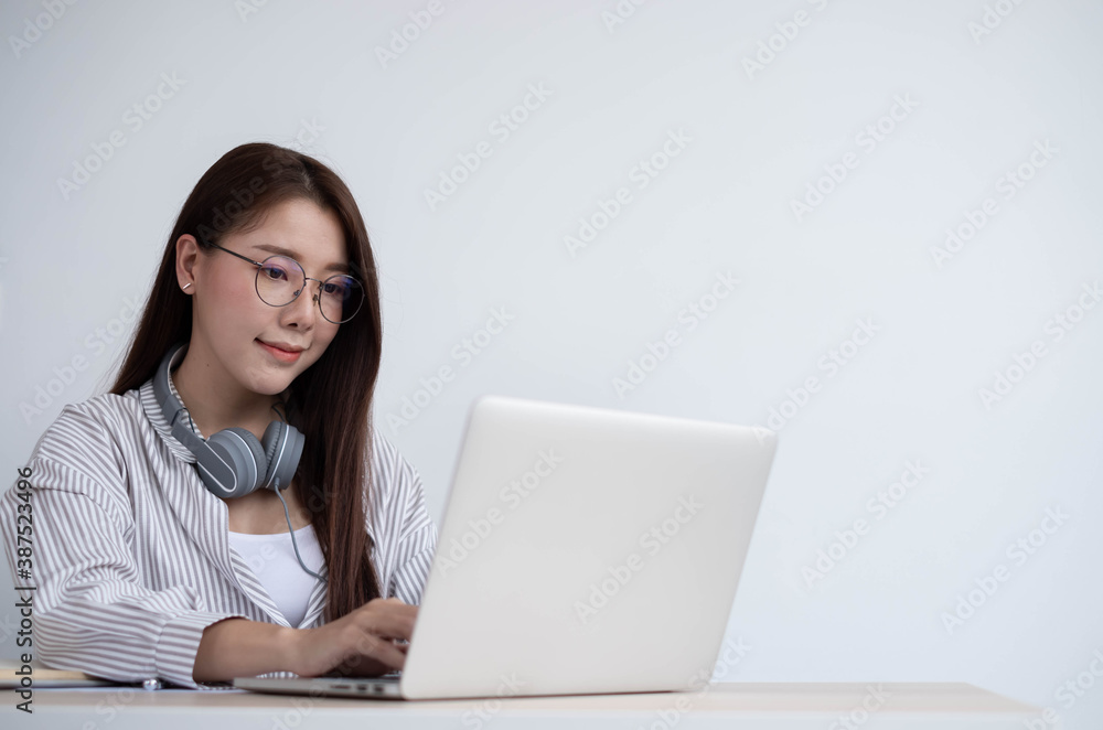 Young Asian women wear headphones using their laptop inside the office, working for online lessons o