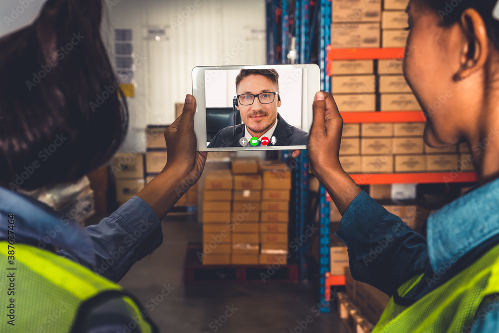 Warehouse staff talking on video call at computer screen in storage warehouse . Online software tech