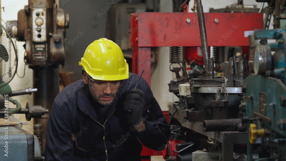 Factory worker talking on portable radio while inspecting machinery parts . Industrial and engineeri