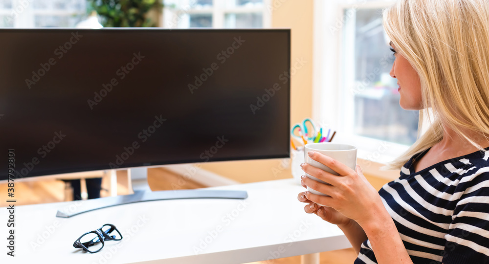 Young woman sitting at her desk in front of big monitor