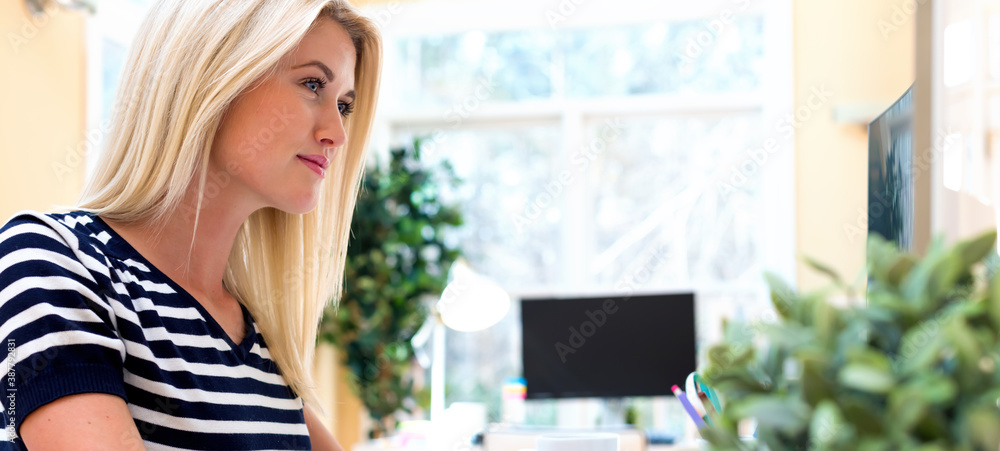 Happy young woman sitting at her desk in front of the computer