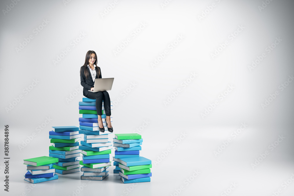 Young businesswoman with laptop sitting on colored books.