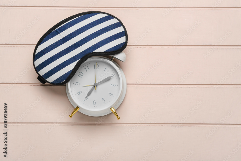 Alarm clock and sleeping mask on wooden background