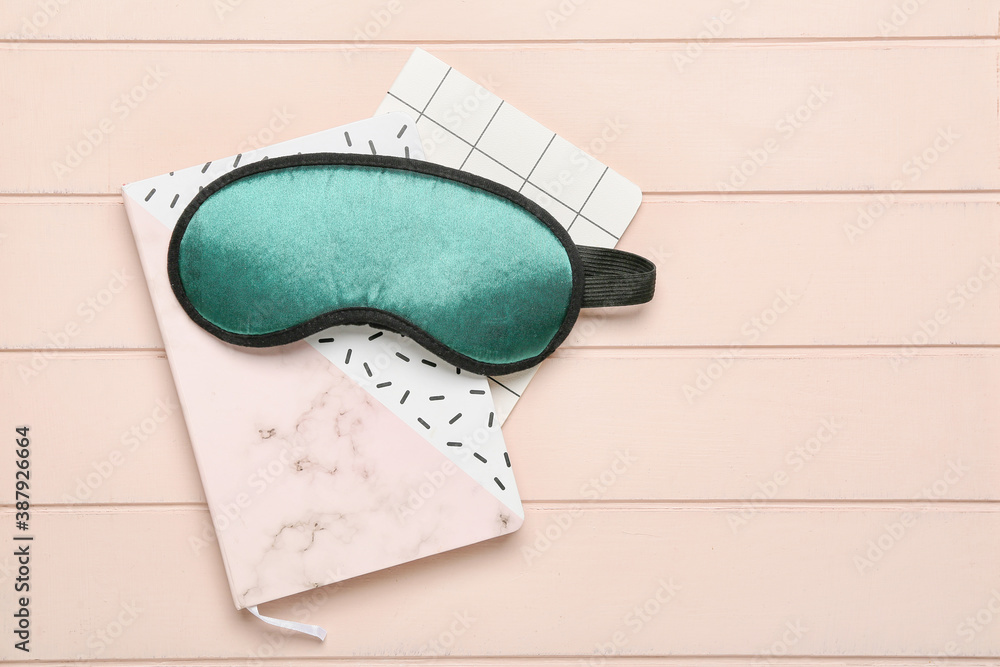 Sleeping mask and notebooks on wooden background