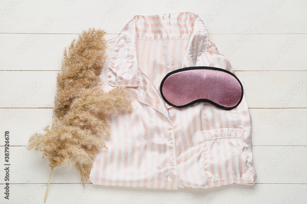 Sleeping mask and pajamas on white wooden background