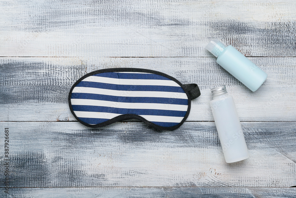 Sleeping mask and cosmetics on wooden background