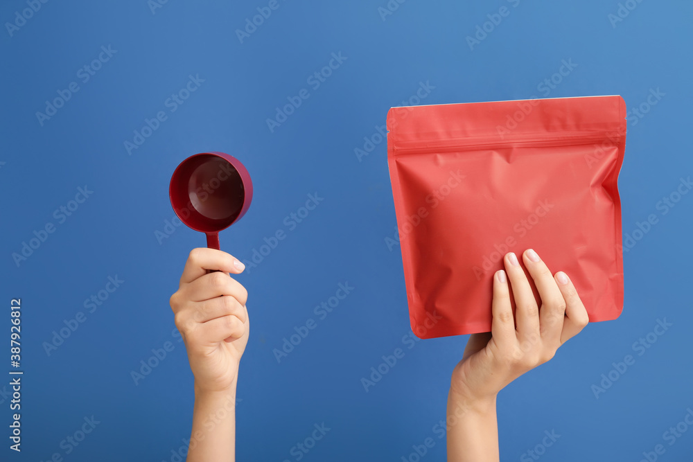 Hands with coffee bag and scoop on color background