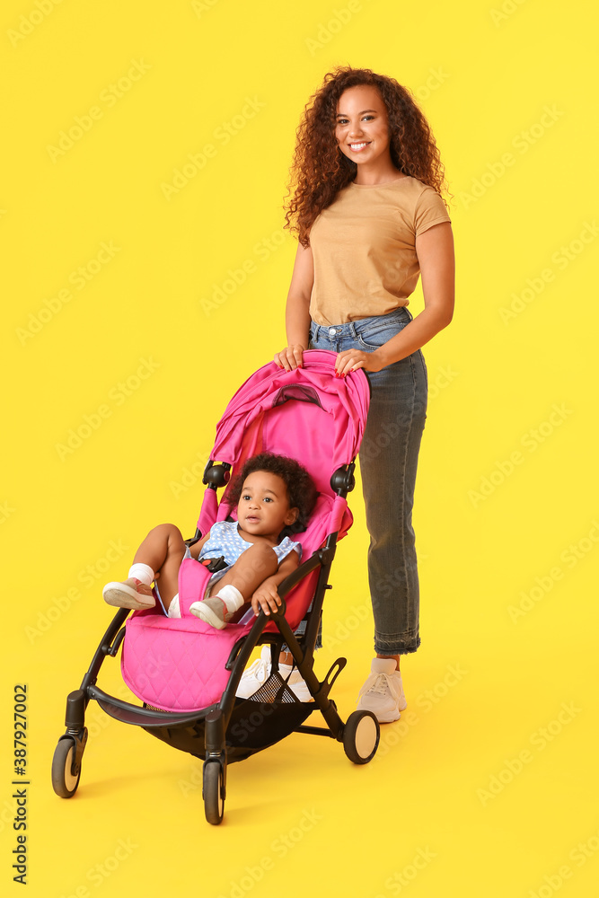 African-American woman and her cute baby in stroller on color background