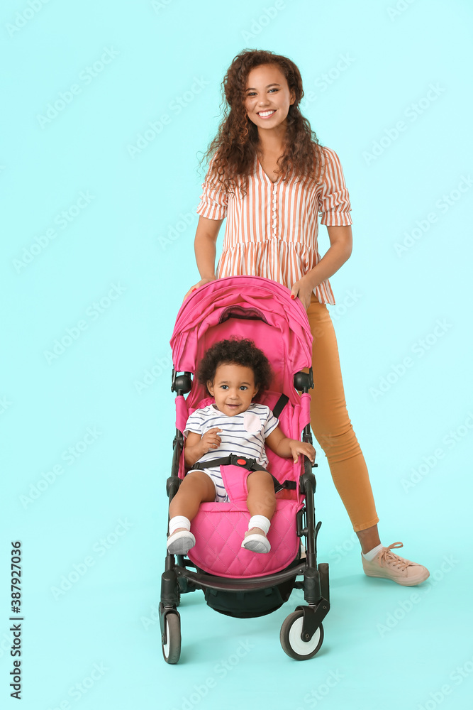 African-American woman and her cute baby in stroller on color background