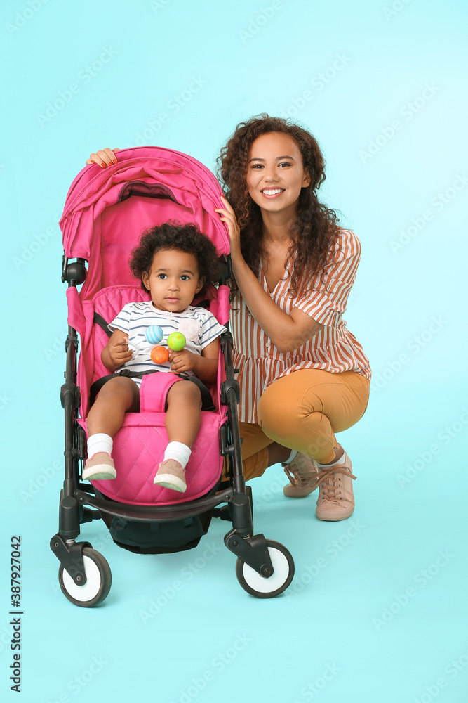 African-American woman and her cute baby in stroller on color background