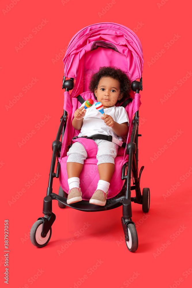 Cute African-American baby in stroller on color background