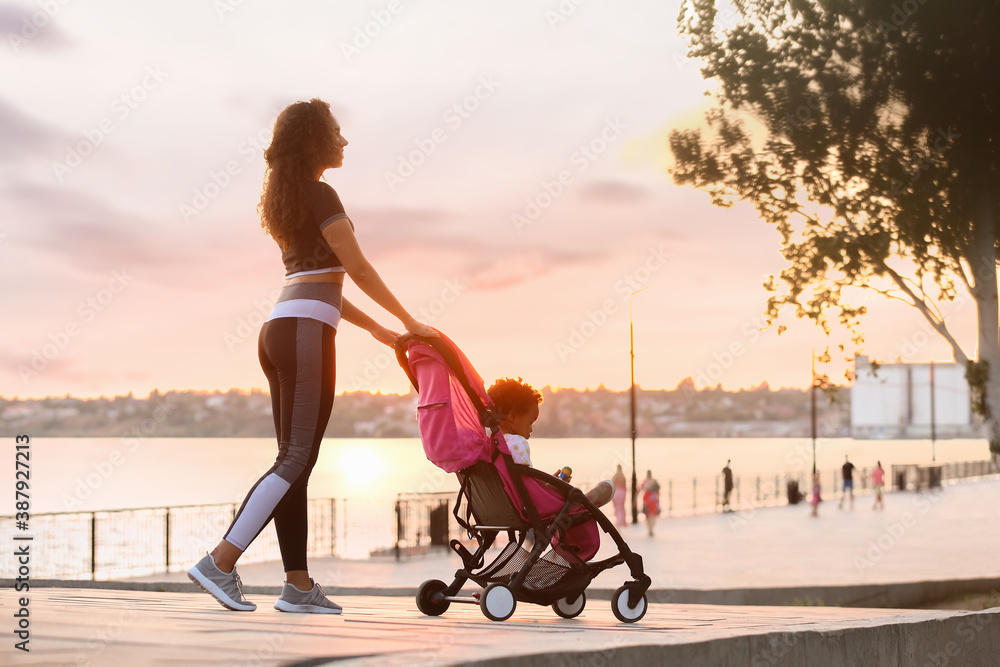 Sporty African-American woman and her cute baby in stroller outdoors