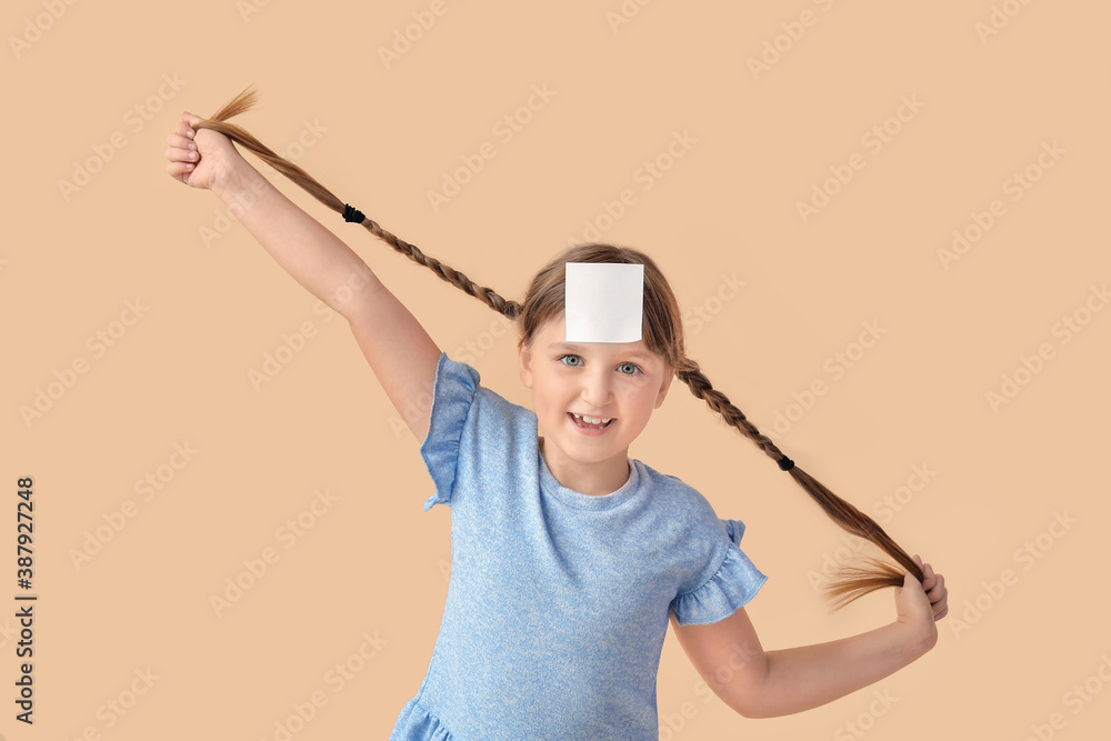 Little girl with blank note paper on her forehead against color background